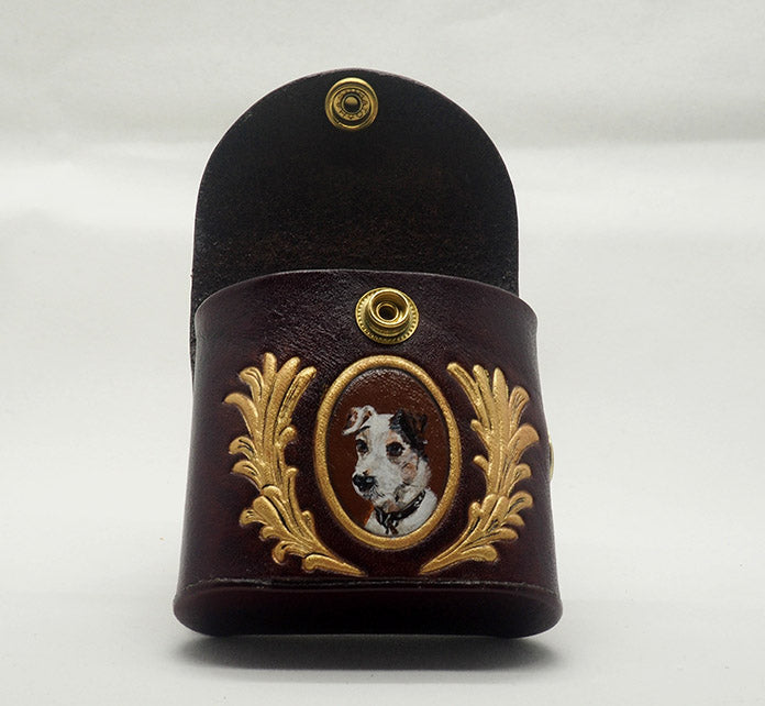 Mahogany leather dog waste bag dispenser with brass snap hardware. Bag is open to showcase the dark brown interior. Design features a portrait of a jack russell terrier dog against an umber colored background with a gold frame, wreathed with gold laurels.