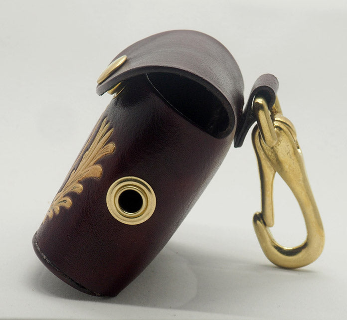 Mahogany leather dog waste bag dispenser with solid brass hardware. From this side, you can see the brass grommet through which the bags dispense as well as the brass halter-style clip.