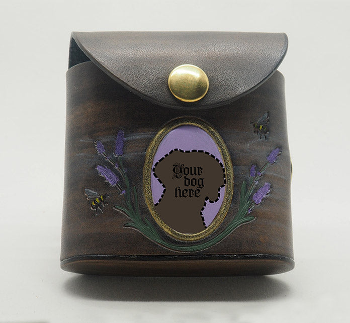 Grey leather dog waste bag dispenser with brass snap hardware. The front features a portrait frame with an empty space and the words "your dog here" written in it, against a lavender background with a gold frame, with lavender and bees wreathing the frame.
