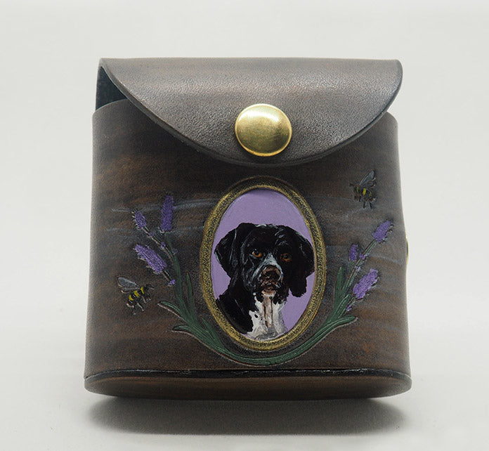Grey leather dog waste bag dispenser with brass snap hardware. Design features a portrait of a german shorthaired pointer dog against a lavender colored background with a gold frame, with lavender and bees wreathing the frame.