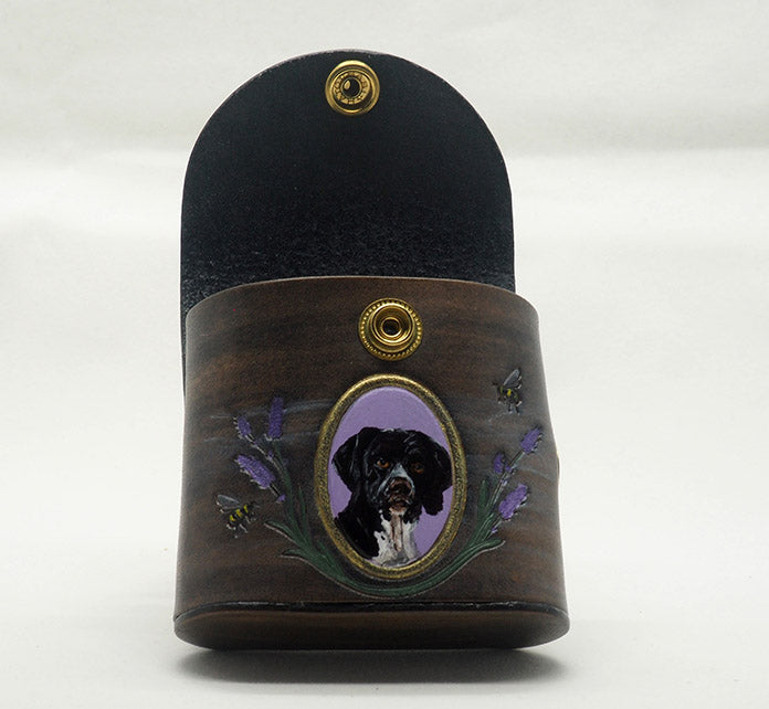 Grey leather dog waste bag dispenser with brass snap hardware; photographed with the top unsnapped to display the darker color of the interior. The exterior has a portrait of a german shorthaired pointer dog against a lavender background with a gold frame, with lavender and bees wreathing the frame.