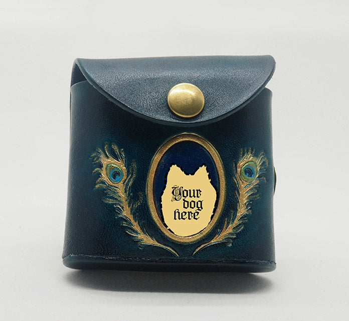 Peacock teal leather dog waste bag dispenser with brass snap hardware. Design features a gold portrait frame with a monastral blue colored background and the text "Your dog here," wreathed in gold peacock feathers.