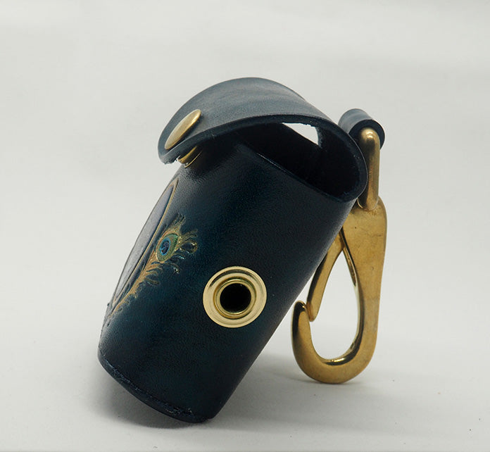 Peacock teal leather dog waste bag dispenser with solid brass hardware. Pictured from the side to show the brass grommet where the bags dispense and the halter-style clip.
