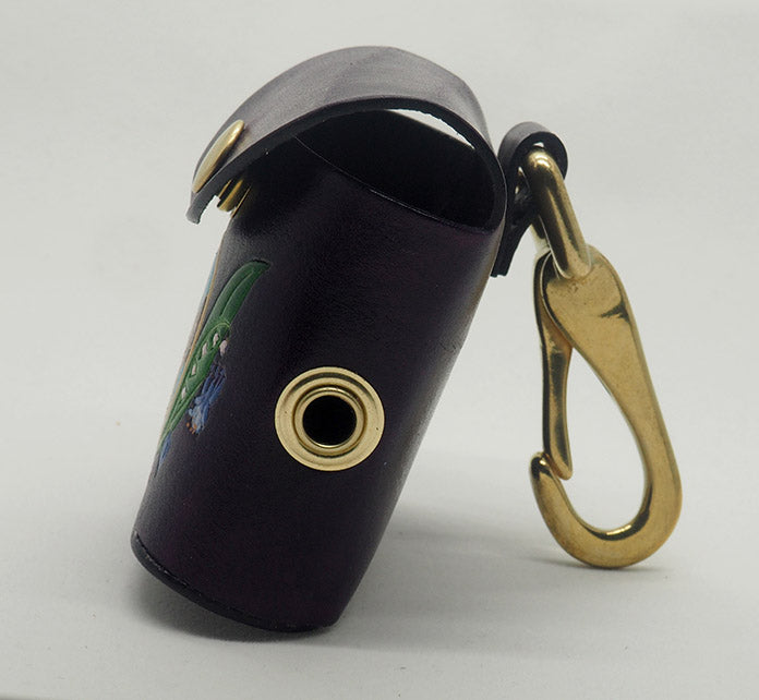 Eggplant purple leather dog waste bag dispenser with solid brass hardware. This side photo displays the brass grommet from where the bags dispense and the halter-style clip.